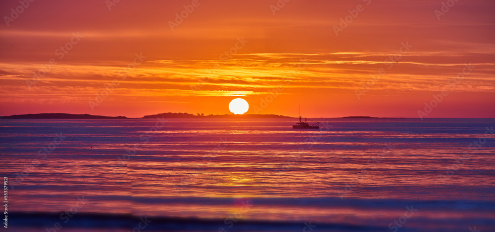 Golden light over east coast ocean with sunrise and detail of sun and fishing ship in distance