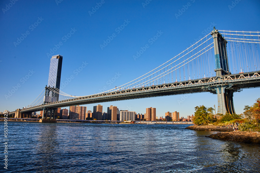 View of entire Manhattan Bridge from Brooklyn in New York City over waters with blue sky