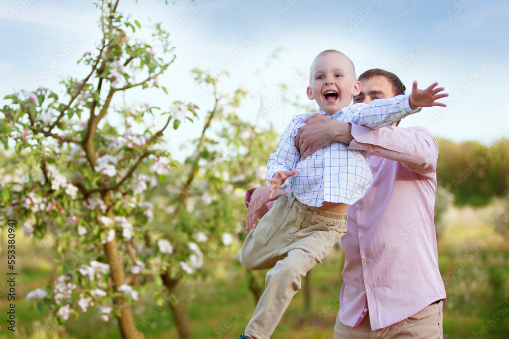 Fototapeta premium Happy father with a little son in a blooming garden. Dad's Day. Throw the child up.