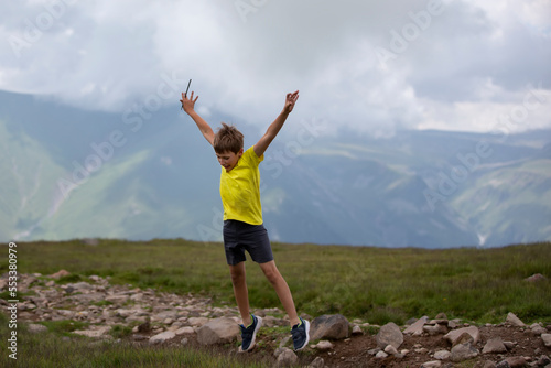 Happy boy against the backdrop of a mountain landscape, joyfully jumping, enjoying life.