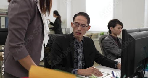 asian male worker overwhelmed by a stack of more paperwork from his boss while working in the office. he checks the document with a stressed face