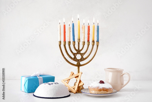 Menorah with doughnut, jug, Jewish hat and gift for Hannukah celebration on white background photo