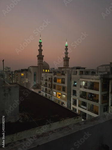 A beautiful roof top view of a beautiful mosque with great lightning, surrounded by a lot of other dense buildings, also with a dark evening sky up above. photo