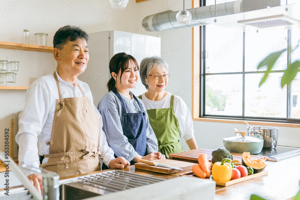キッチンで料理する高齢者夫婦と若い日本人（家事代行・介護）
