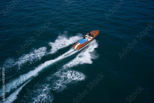 Classic italian wooden boat with people moving fast on the water, top view. Top view of a wooden powerful motor boat. Luxurious wooden boat moves fast on dark water.