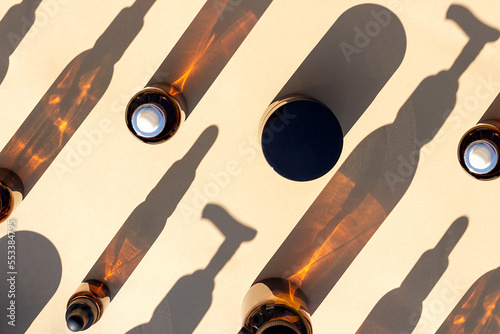 Pattern made with brown glass bottle of cosmetic products and strong shadow on beige background, as a backdrop or texture. Creative layout for your design