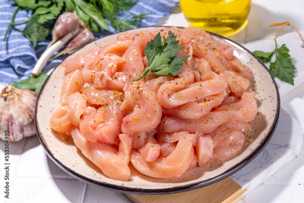 Cooking diet white poultry meat background. Fresh sliced chicken strips raw for cooking, with spices, herbs, on a white tile background top view copy space Cooking diet white poultry meat background. Fresh sliced chicken strips raw for cooking, with spices, herbs, on a white tile background top view copy space