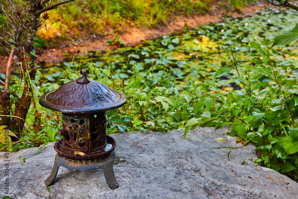 Small metal lantern by lily pond on rocks Small metal lantern by lily pond on rocks