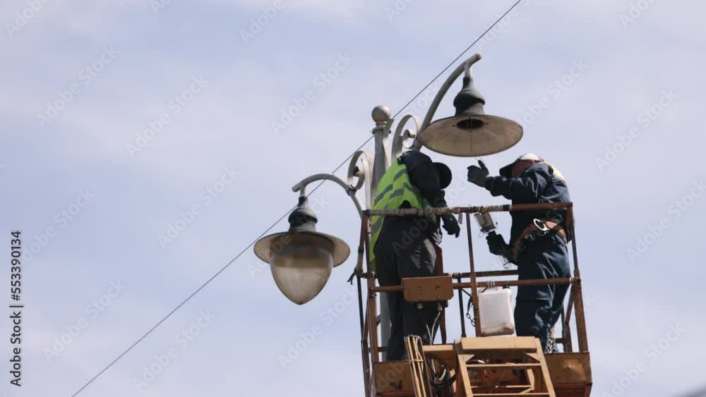repair street lamp, lift bucket, fix light. Worker is fixing street