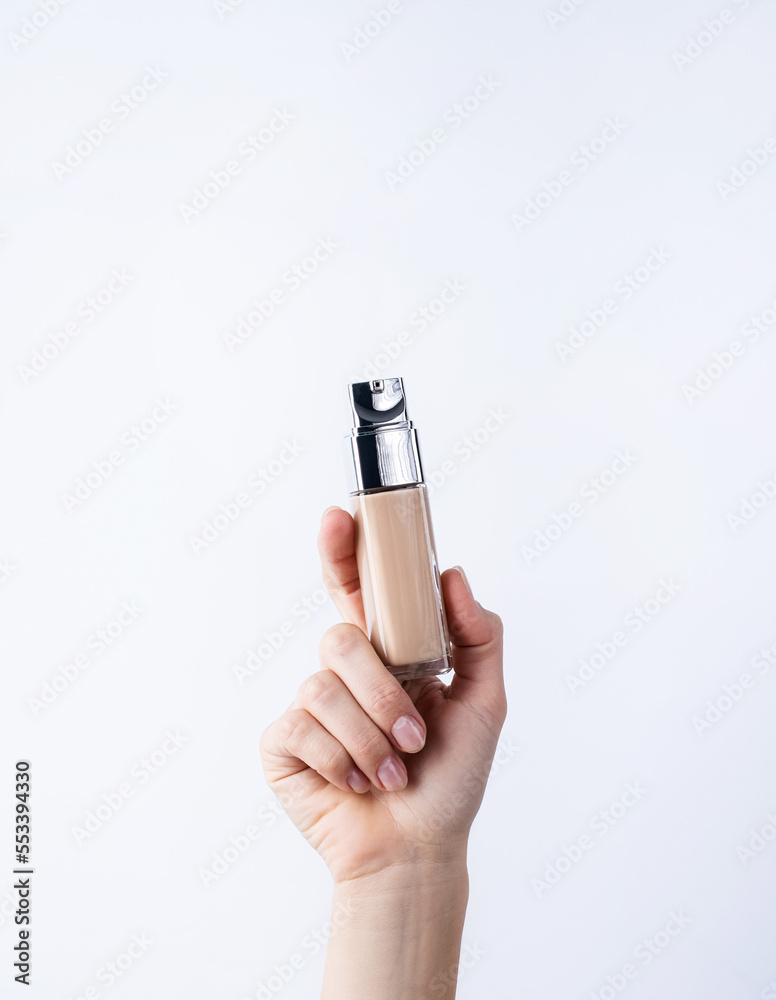 Woman hand holding glass bottle with foundation cream on light gray background Woman hand holding glass bottle with foundation cream on light gray background