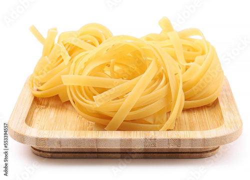 Raw fettuccine pasta on a wooden plate, white background