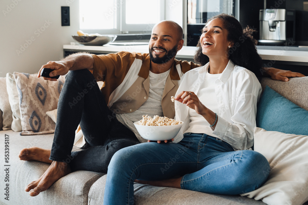 © Drobot Dean - African american couple watching TV while sitting on sofa © Drobot Dean - African american couple watching TV while sitting on sofa