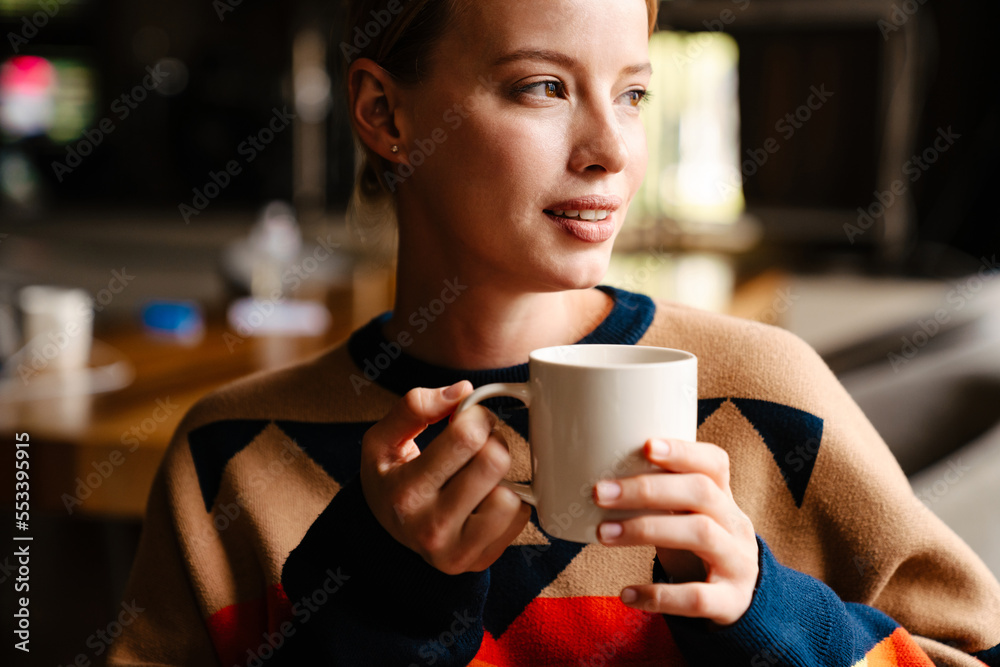 Pensive woman drinking tea and looking aside while sitting in cafe Pensive woman drinking tea and looking aside while sitting in cafe