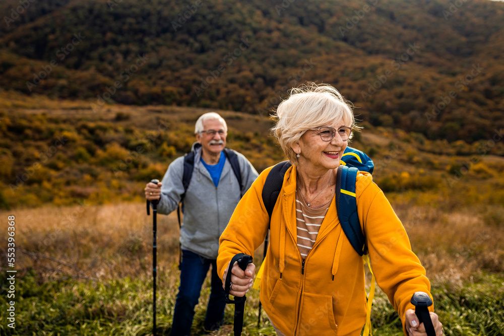 Active senior couple with backpacks hiking together in nature on autumn day.