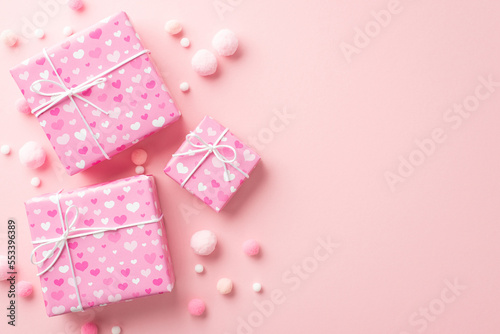 Valentine's Day concept. Top view photo of present boxes in wrapping paper with heart pattern and fluffy pompons on isolated pastel pink background with copyspace © ActionGP