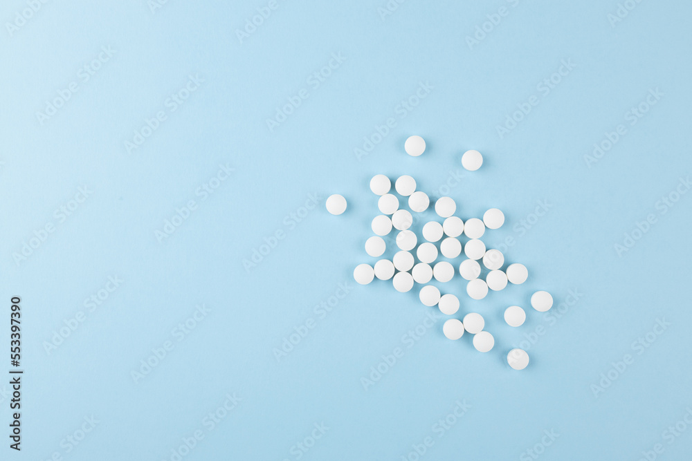 Health and pharmacy remedies for prevent and teraphy disease and illness background - heap of white pills on soft light pastel blue color, top view,  copy space.