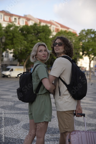 Happy tourist couple looking back. Man and woman with backpacks and suitcases. Portrait, travelling concept