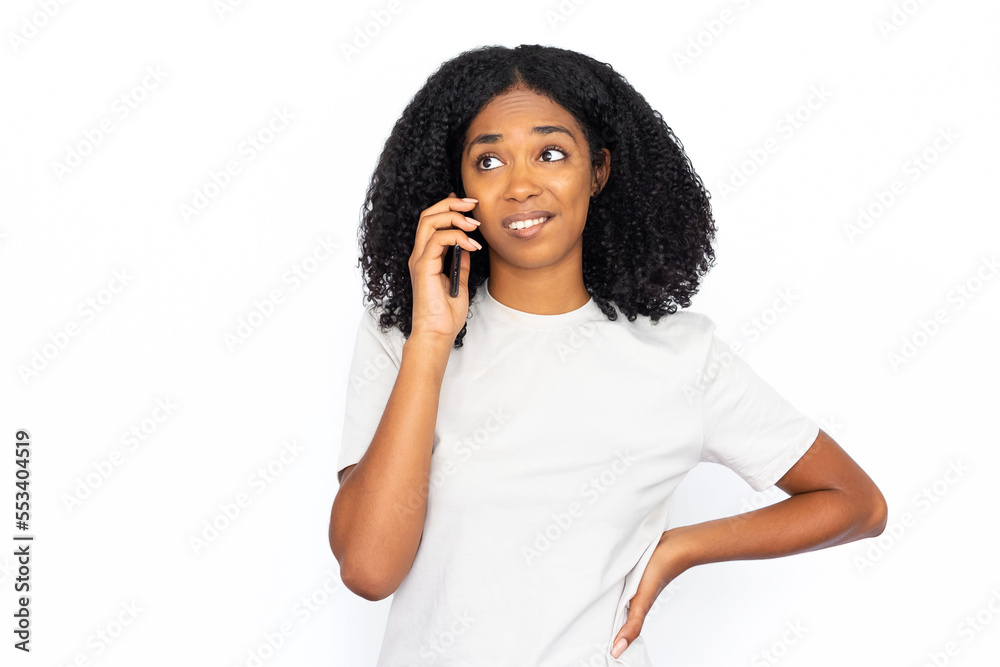 Confused African American woman talking on phone. Upset young female model with dark curly hair in white T-shirt looking away, unsure how to answer. Modern technology, communication concept