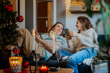 Young cheerful happy lesbian couple spending time at home on sofa hugging during Christmas holidays
