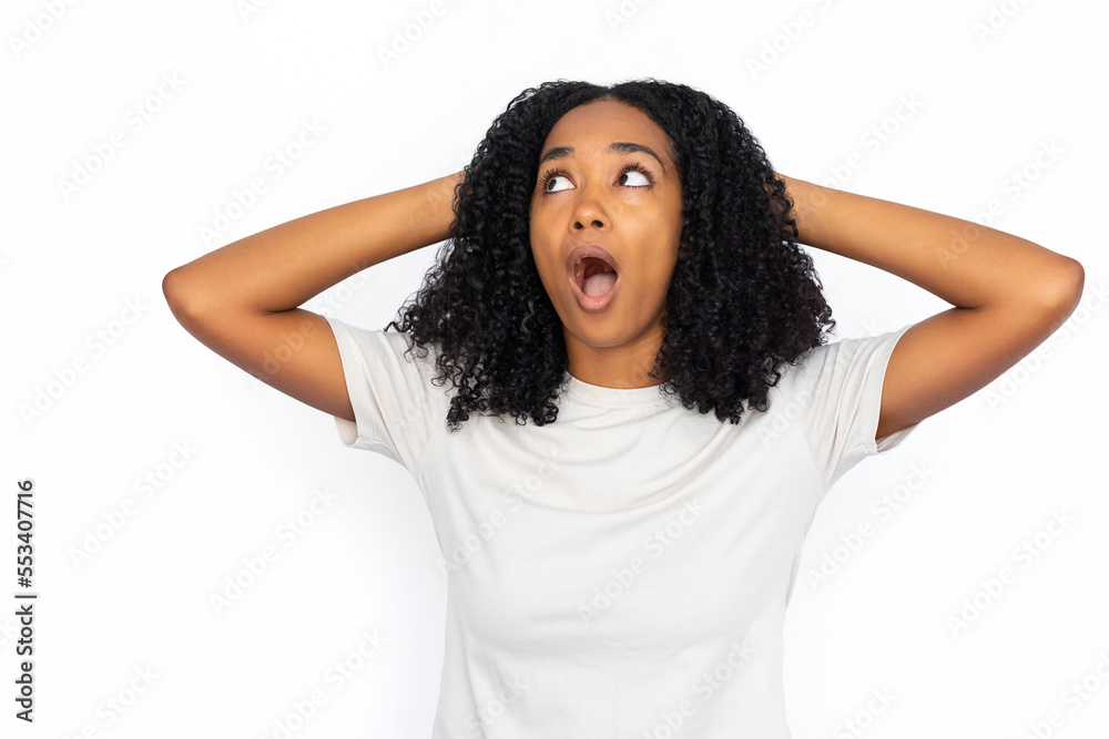 Shocked African American woman with hands on head. Portrait of amazed young female model with dark curly hair in white T-shirt looking away with open mouth, pulling hair. Shock concept Shocked African American woman with hands on head. Portrait of amazed young female model with dark curly hair in white T-shirt looking away with open mouth, pulling hair. Shock concept
