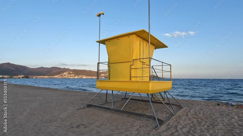 Watchtower on a beach. Yellow watchtower on a wide sand beach. Yellow lifeguard tower with the blue ocean in the background. Waves hitting the beach behind an emtpy yellow lifeguard post. Watchtower on a beach. Yellow watchtower on a wide sand beach. Yellow lifeguard tower with the blue ocean in the background. Waves hitting the beach behind an emtpy yellow lifeguard post.