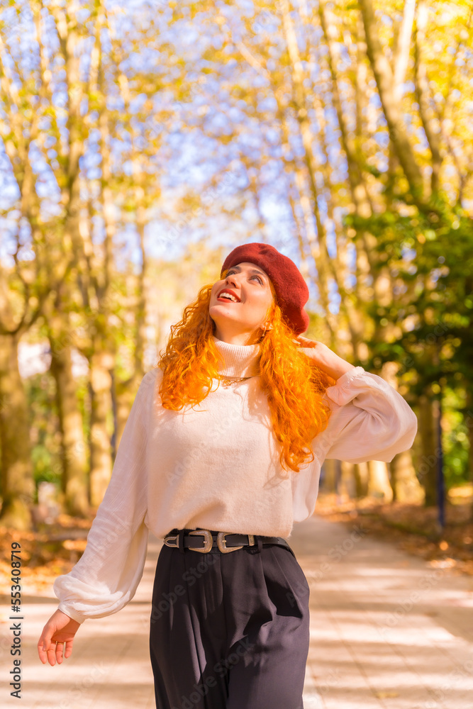 Red-haired woman in a beret walking through a city forest park at sunset, vertical photo Red-haired woman in a beret walking through a city forest park at sunset, vertical photo