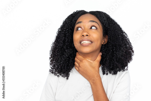 Frustrated multiracial woman choking herself. Portrait of sick young female model with dark curly hair in white T-shirt looking away with hand on neck, suffering from sore throat. Sickness concept