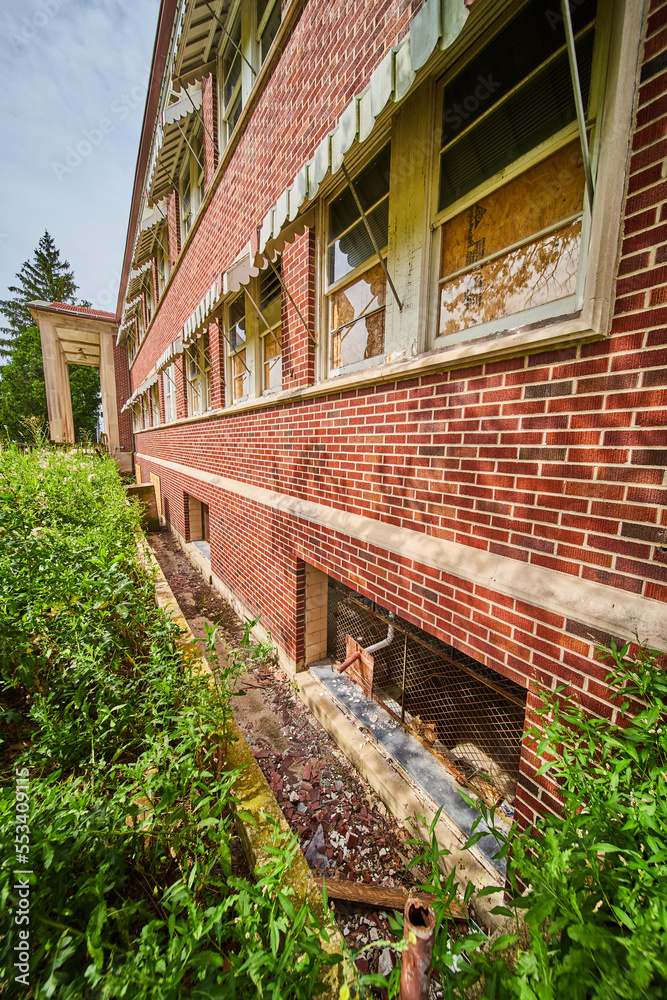 Detail of exterior wall of abandoned brick building with broken glass and overgrown fields