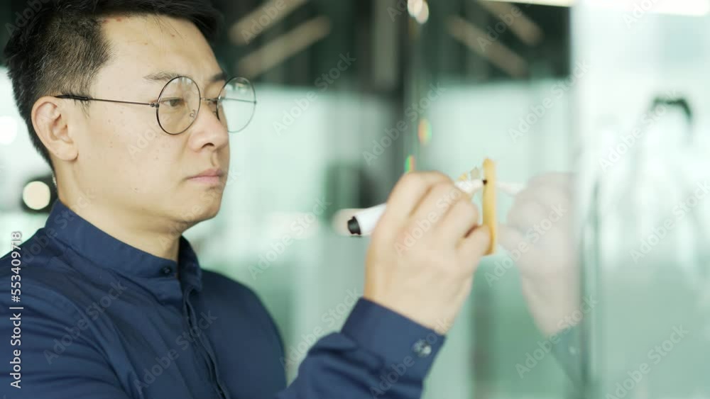 Busy asian businessman IT programmer with glasses work write idea on paper sticker sticky notes on glass wall develops a strategy for startup enterprise financial growth at modern office workplace 