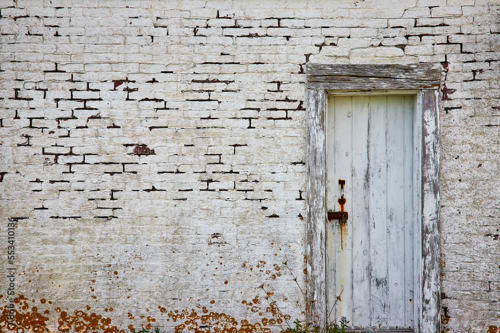 Abandoned white brick building with old decaying wood door and lichen Abandoned white brick building with old decaying wood door and lichen