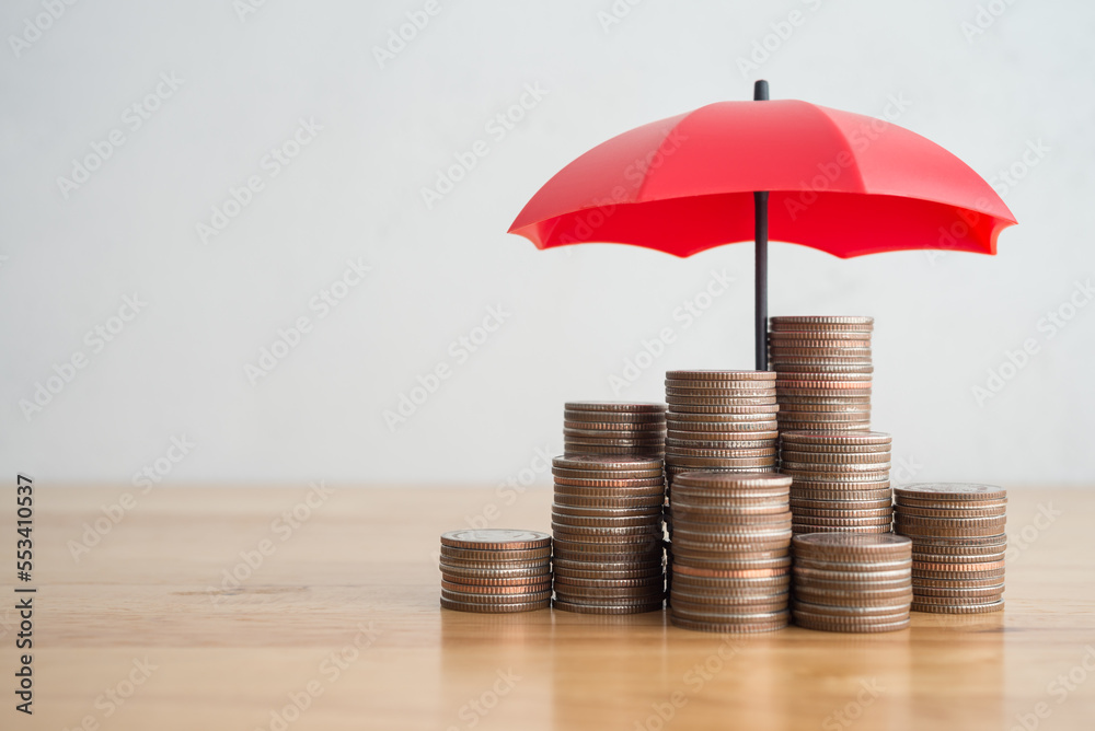 Stacked coins is protected by red umbrella on wooden table white wall background copy space. Assets wealth, money saving or money investment protection, security by insurance concept. Risk management. - obrazy, fototapety, plakaty 