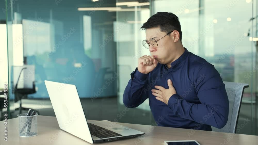 Sick asian businessman employee coughing a lot while sitting at the desk in modern business centre alone Unhealthy mature male with glasses getting bronchitis flu virus symptom at workplace indoors Sick asian businessman employee coughing a lot while sitting at the desk in modern business centre alone Unhealthy mature male with glasses getting bronchitis flu virus symptom at workplace indoors
