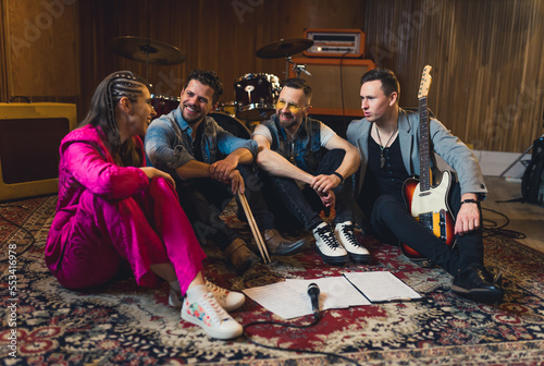 Band members - drummer, vocalist and two guitarists - learning a new song, sitting on the floor with notes. Full-length indoor photo. High quality photo