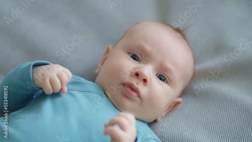 Cute two-month-old baby in blue clothes looks into camera. Sweet newborn boy lies on the sofa. Shooting from the upper angle of a chubby male kid. Beautiful infant boy with blue eyes.