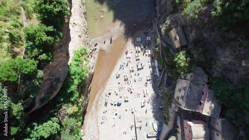 A rising aerial shot of tourists tanning in the sun. The narrow, hidden pebble beach at the picturesque Fiordo di Furore is a must-see destination for travelers to the Amalfi Coast in Italy.