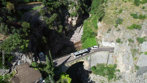 A cinematic aerial establishing shot moving over a bridge and revealing the picturesque Fiordo di Furore pebble beach, a scenic vacation destination for tourists on the Amalfi Coast in Italy. photo