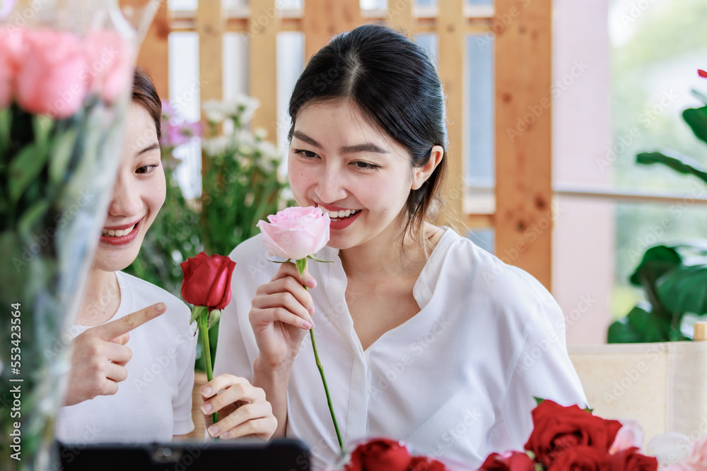 Millennial two Asian young professional female flower shopkeeper owner decorator standing holding red roses bunch bouquet in plastic wrapped smiling sending to customer celebrating valentine day