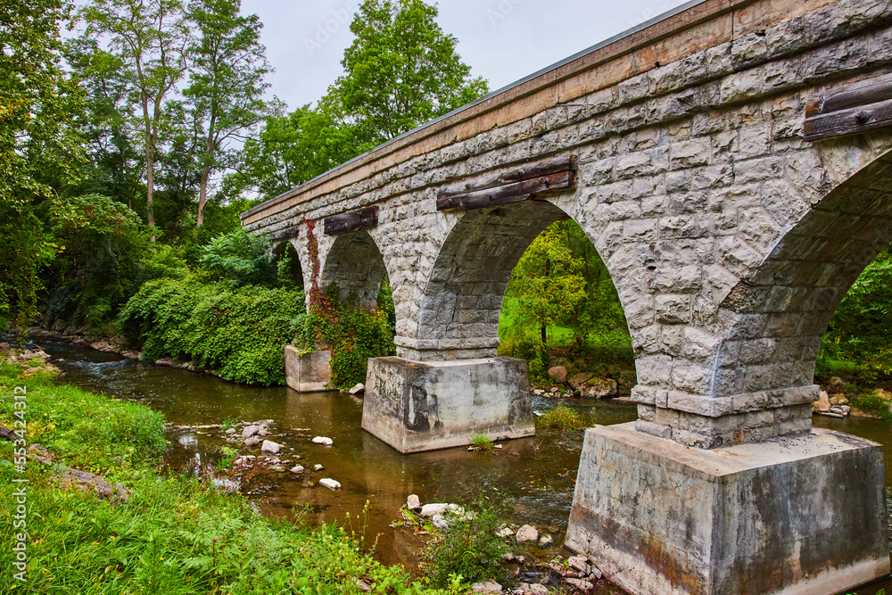 Old stone arch bridge for train tracks over small river