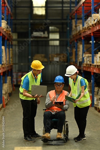 Two young storehouse worker and male manager in wheelchair working on a digital tablet during an inventory check