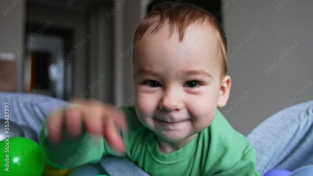 Caucasian one year old toddler plays with balls in soft dry basin. Close up. Baby moves his hands by the toys happily. Caucasian one year old toddler plays with balls in soft dry basin. Close up. Baby moves his hands by the toys happily.