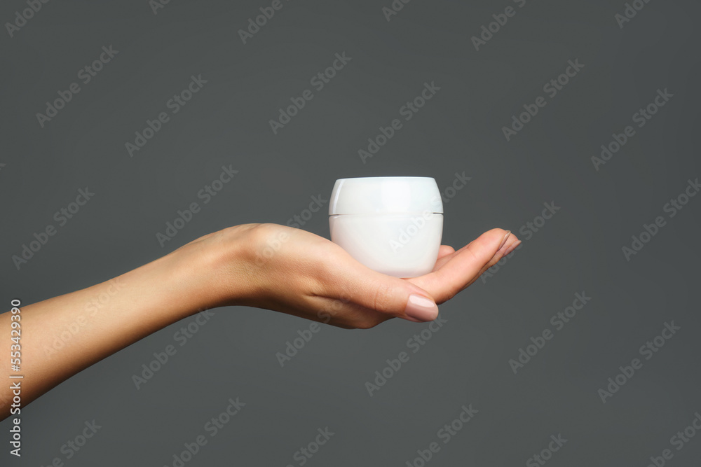Skincare beauty product. Studio photo of female hand is holding a white jar with cream against grey background. Daily care and hygiene routine. Skincare beauty product. Studio photo of female hand is holding a white jar with cream against grey background. Daily care and hygiene routine.