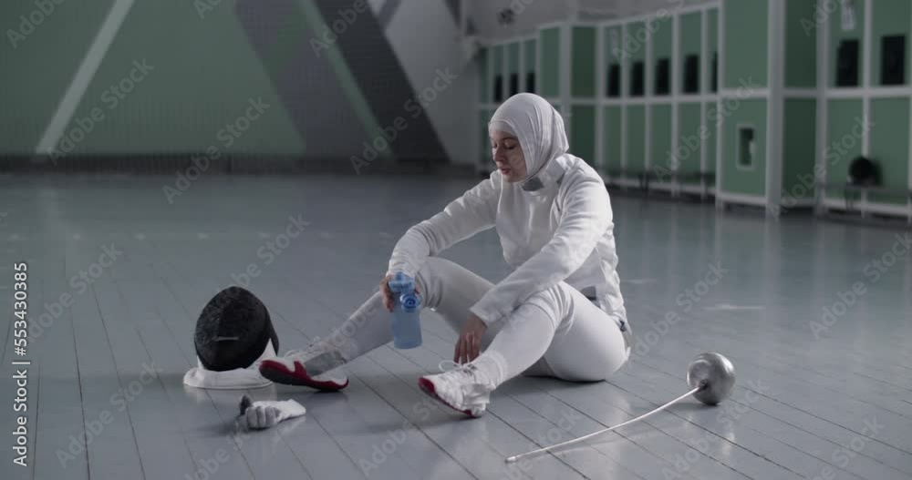 Muslim female fencer drinking water on floor Muslim female fencer drinking water on floor