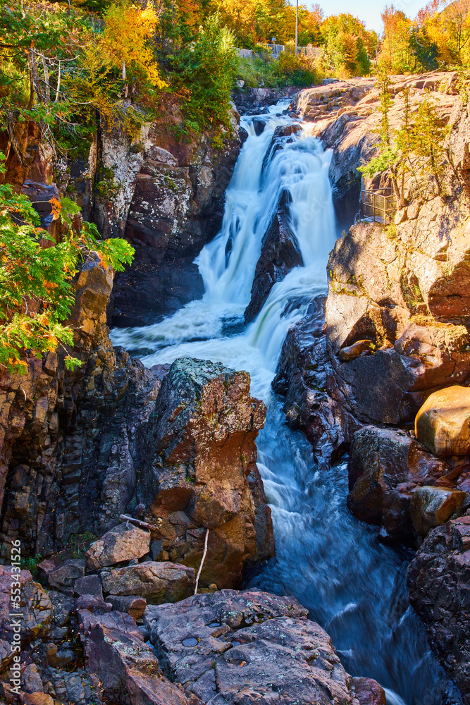 Obraz premium Rocky cliff gorge canyon with large heavy waterfalls and fall forest
