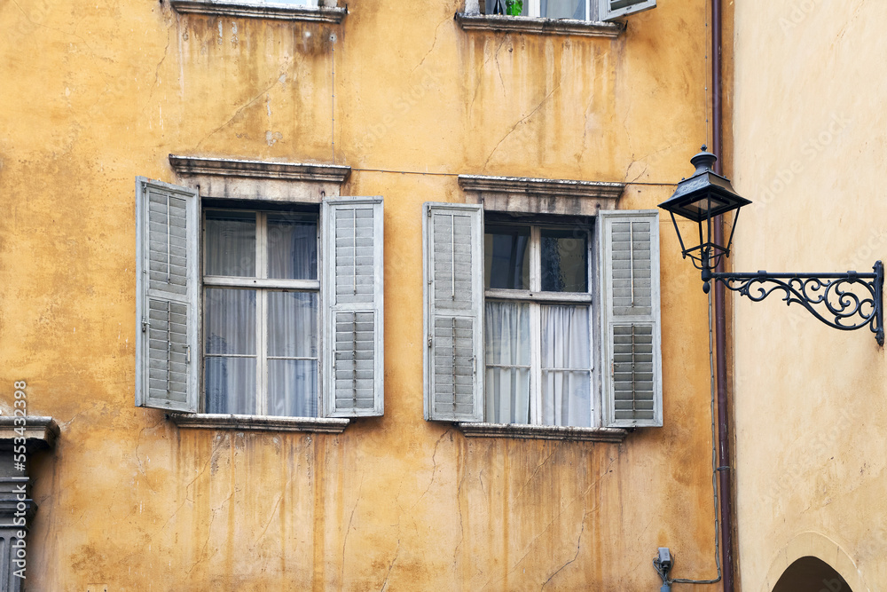 Two Italian windows on the bright yellow wall facade with open grey color classic shutters