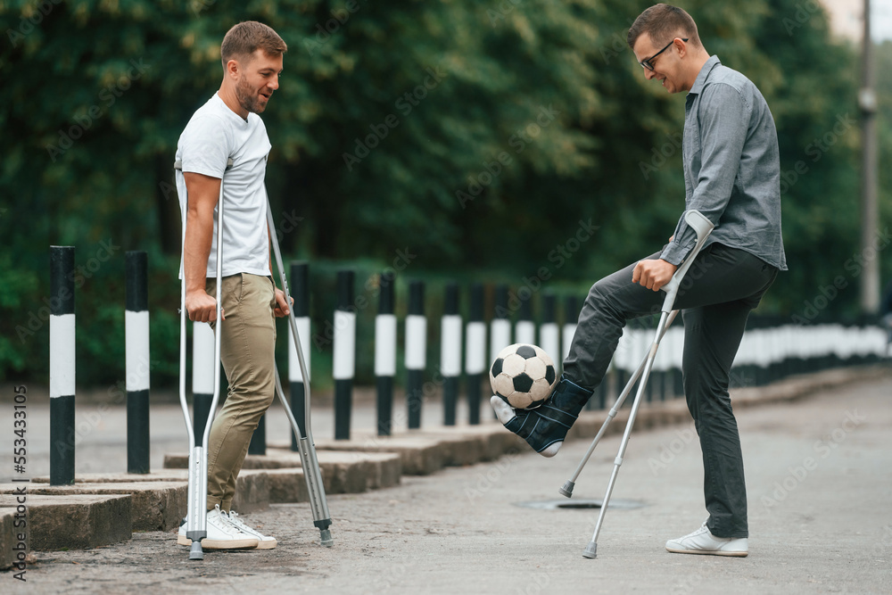 Obraz premium Having fun, playing soccer. Two men with crutches is outdoors on the road