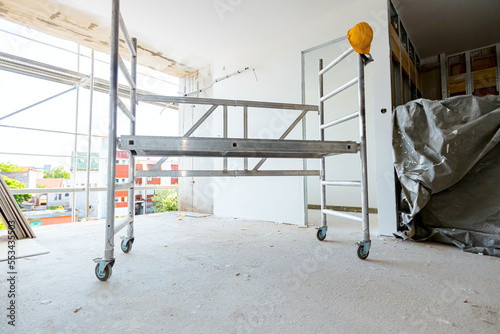 Fototapeta Moveable scaffold with wheels in the building under construction, yellow hardhat
