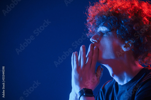 Side view. Young man with curly hair is indoors illuminated by neon lighting