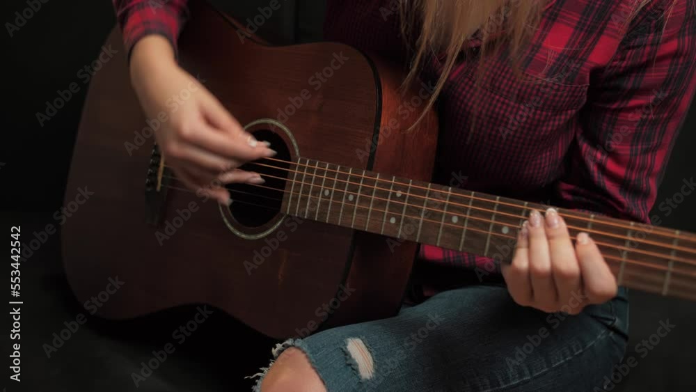 Guitarist plays acoustic guitar at home. The woman strums the chords on the frets and plays the song. Learning to play the classical guitar. Young musician playing guitar in the living room at home. Guitarist plays acoustic guitar at home. The woman strums the chords on the frets and plays the song. Learning to play the classical guitar. Young musician playing guitar in the living room at home.