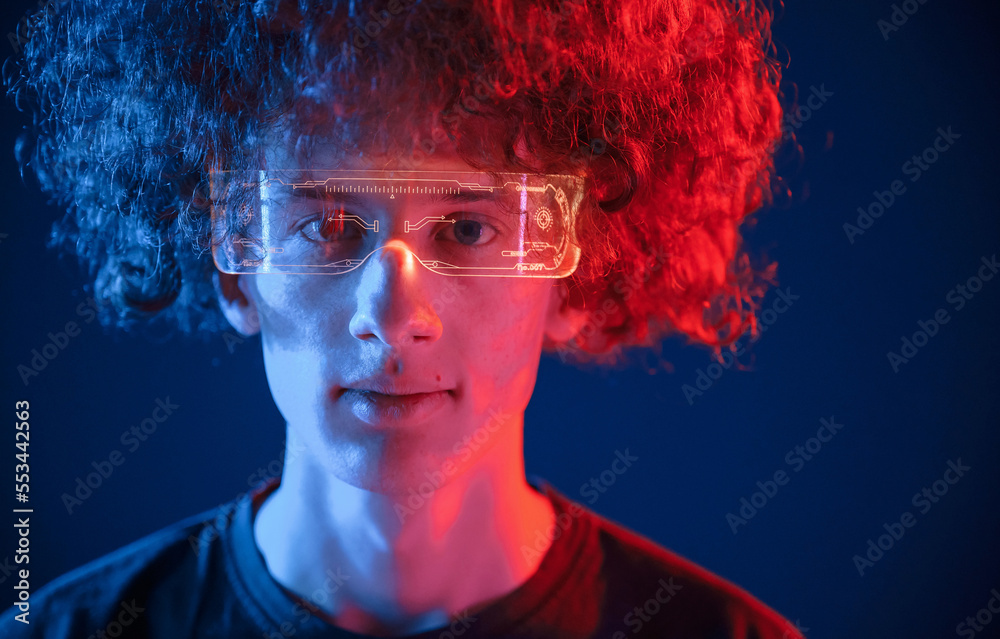 Serious facial expression. Young man with curly hair is indoors illuminated by neon lighting