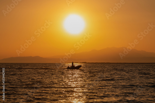 The silhouette of a man in a motor boat, in the sunlight, at sunset